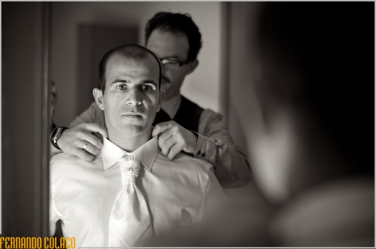 Num espelho, a noivo é ajudado por um amigo com a gravata.