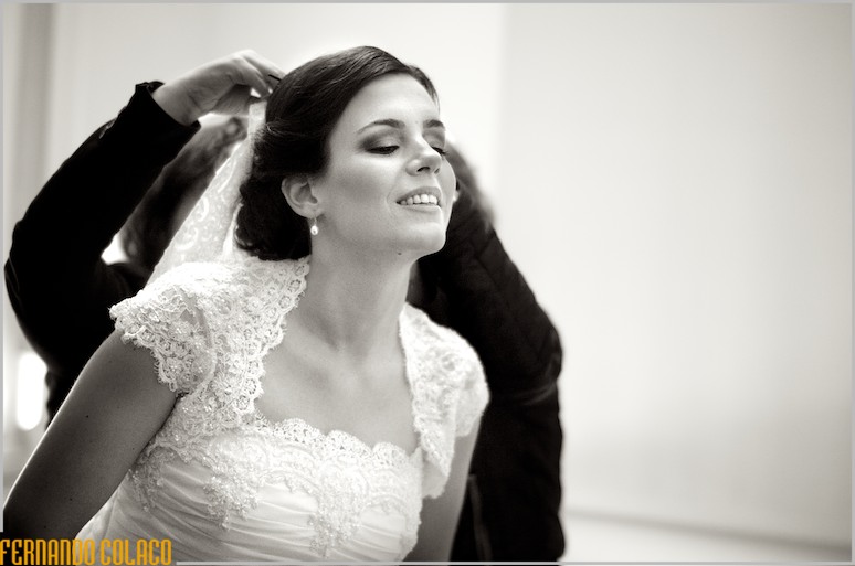 A noiva inclina-se para a frente, quando lhe põem o véu no cabelo.
