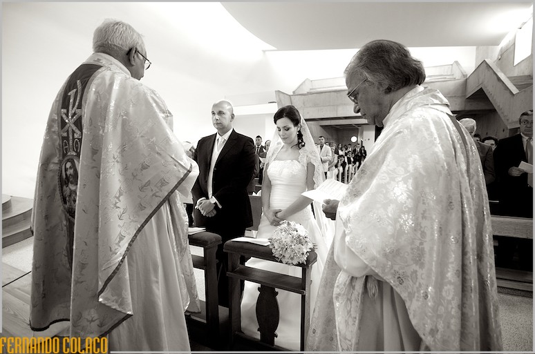 No meio de dois padres, o casal atento ao decorrer da cerimónia do casamento.