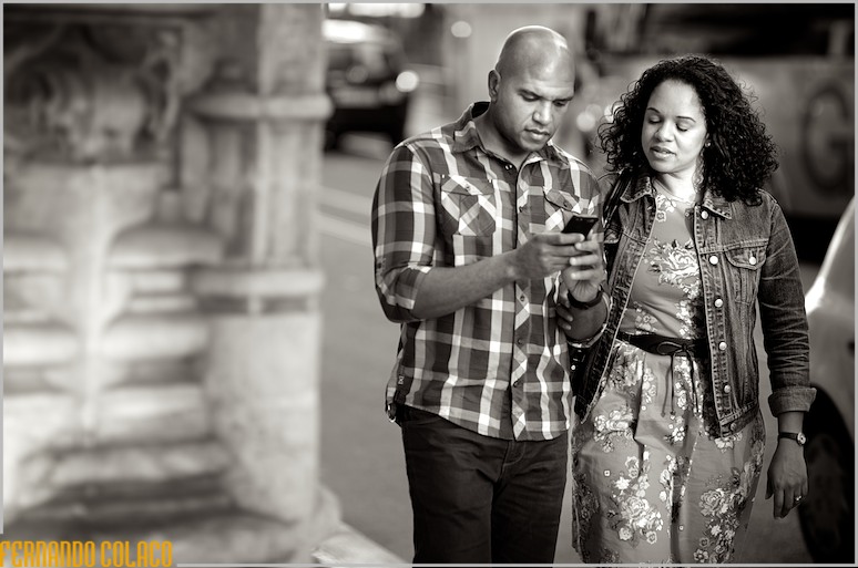While walking in old Lisbon, the couple, in the pre-wedding session, look at something on their cell phone.