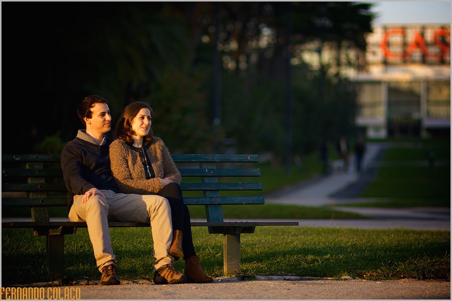 The bride and groom sitting on a bench in the Estoril Casino garden, bathed in sunlight at dusk.