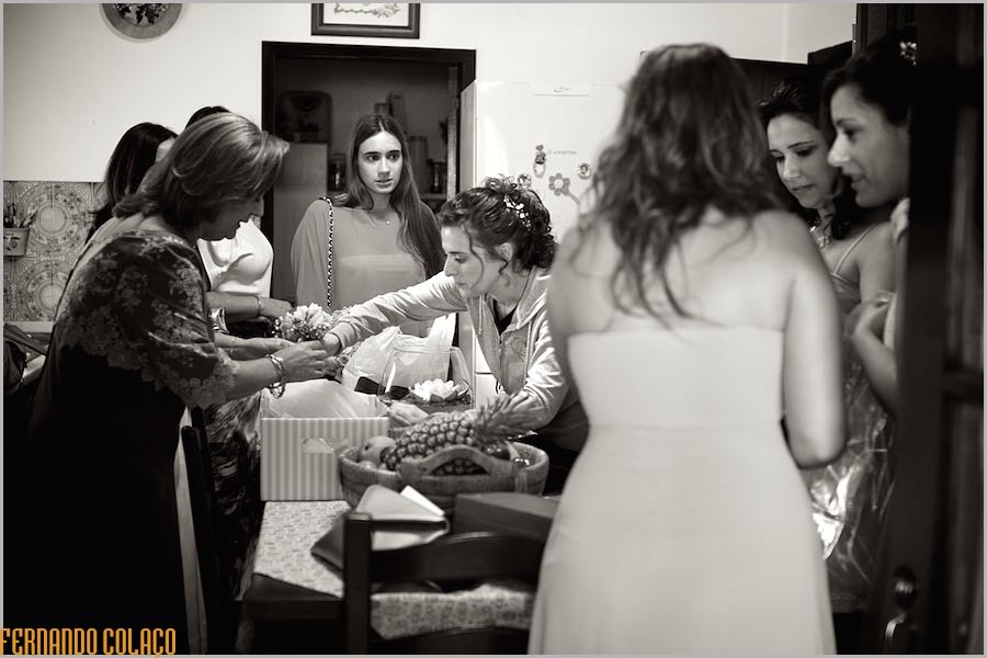 A noiva, antes de vestida para o casamento, no meio de amigas e familiares separando os ramos de flores, sobre uma mesa.