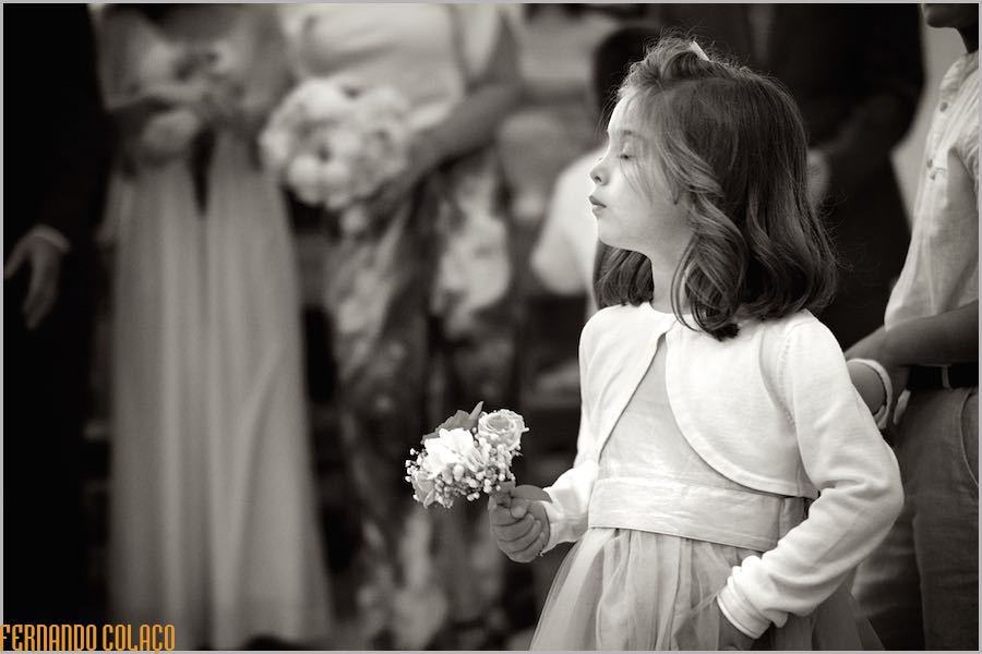 Uma menina, de perfil, com um ramo de flores na mão, na igreja durante a cerimónia do casamento.