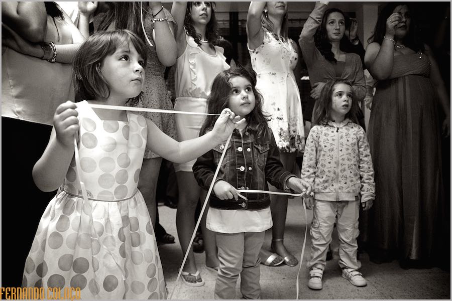 Três meninas olham fixamente para algo que se passa à sua frente, na festa do casamento.