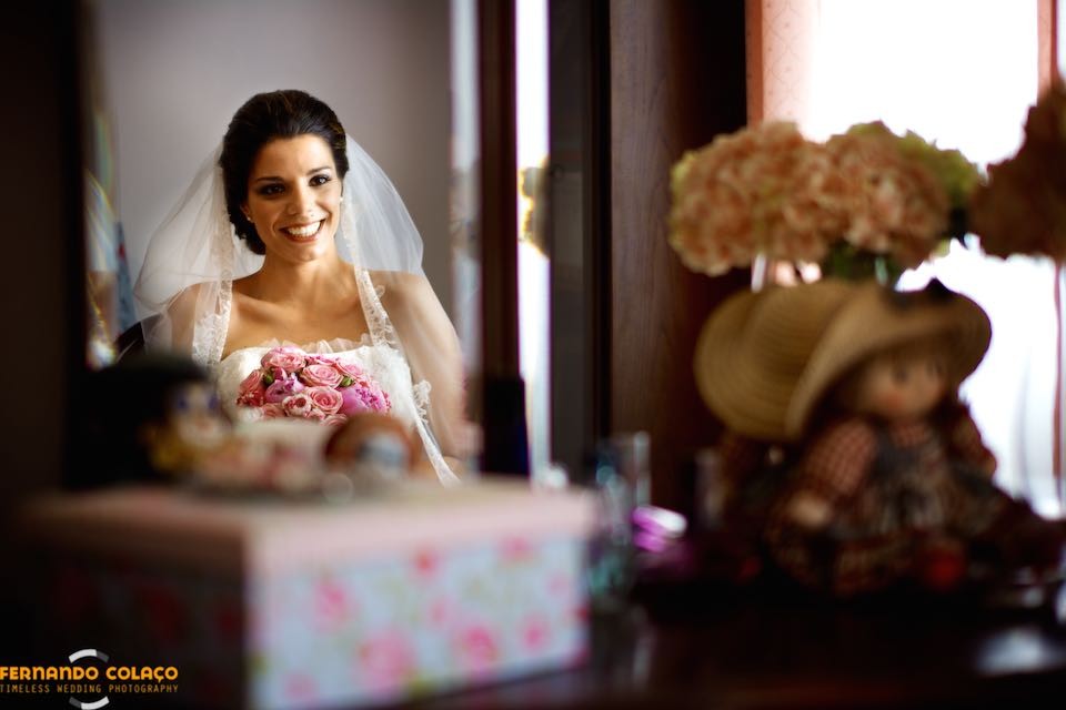 Sentada de frente a um móvel com espelho, a noiva junto de objectos importantes para ela.