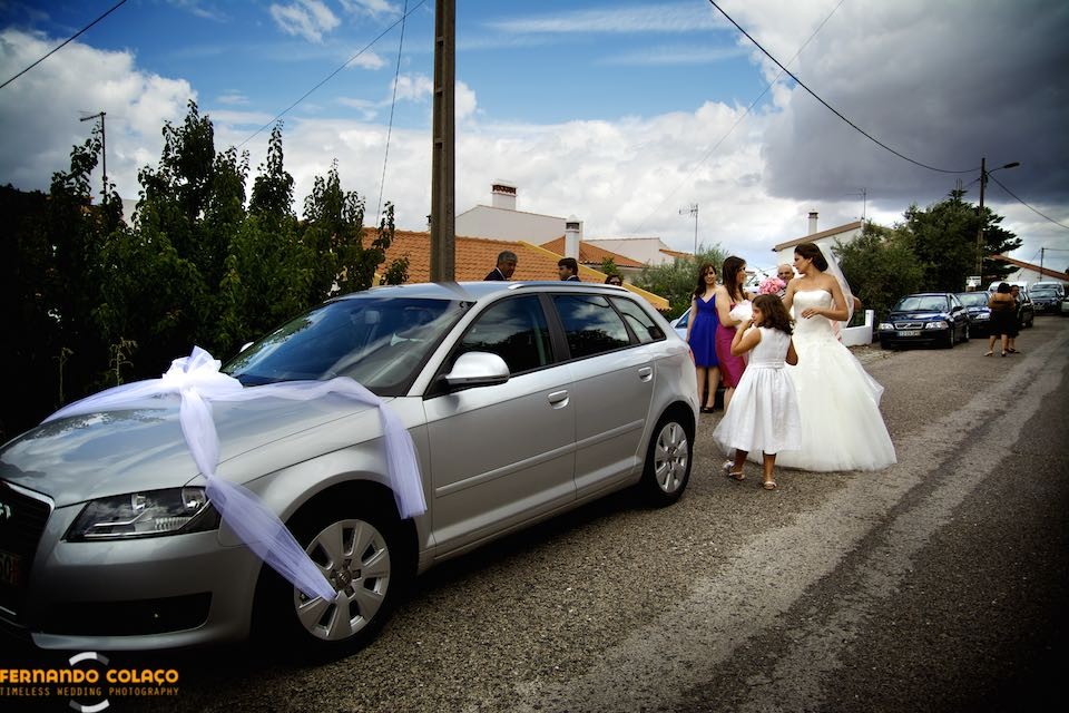Na rua, junto do automóvel, a noiva com familiares prepara-se para partir para a cerimónia do casamento.