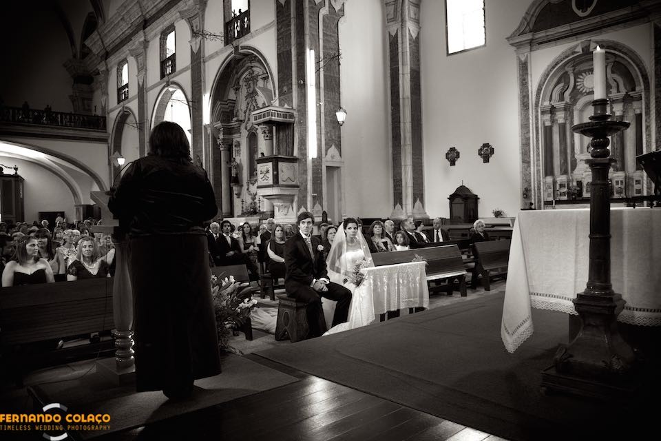 Sentados, durante a cerimónia do casamento, os noivos ouvem uma convidada do casamento ler as escrituras.