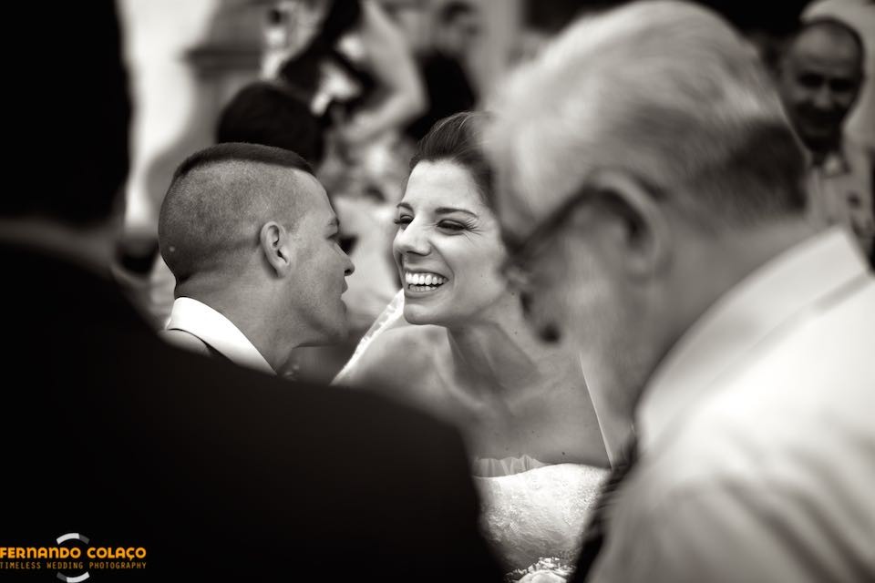 A noiva, a rir, recebe os parabéns de um convidado do casamento à saída da igreja.