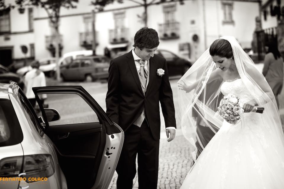 O noivo abre a porta do automóvel para a noiva entrar com o bouquet na mão e partirem para o local da festa do casamento.