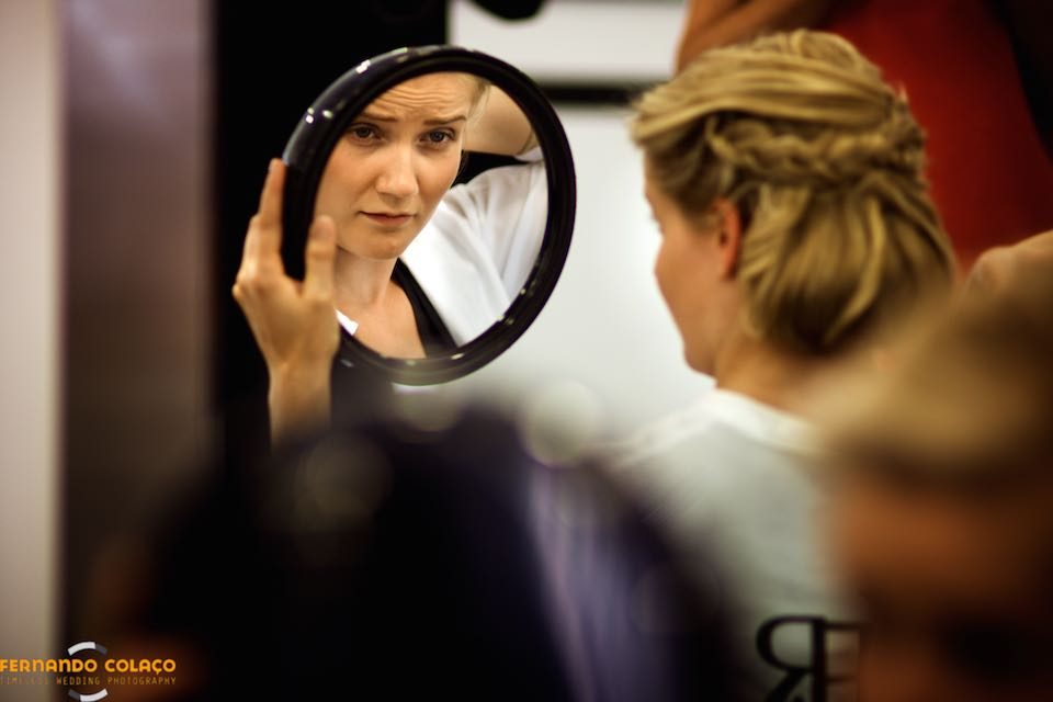 The bride sees herself in a round mirror that she holds in her hand, during her wedding hairstyle.