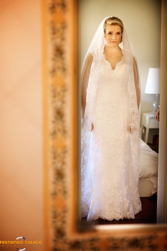 Already dressed and with the veil in her hair, the bride sees herself in the mirror.