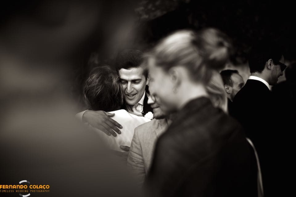 Among the unfocused guests, the groom embraces a wedding guest.