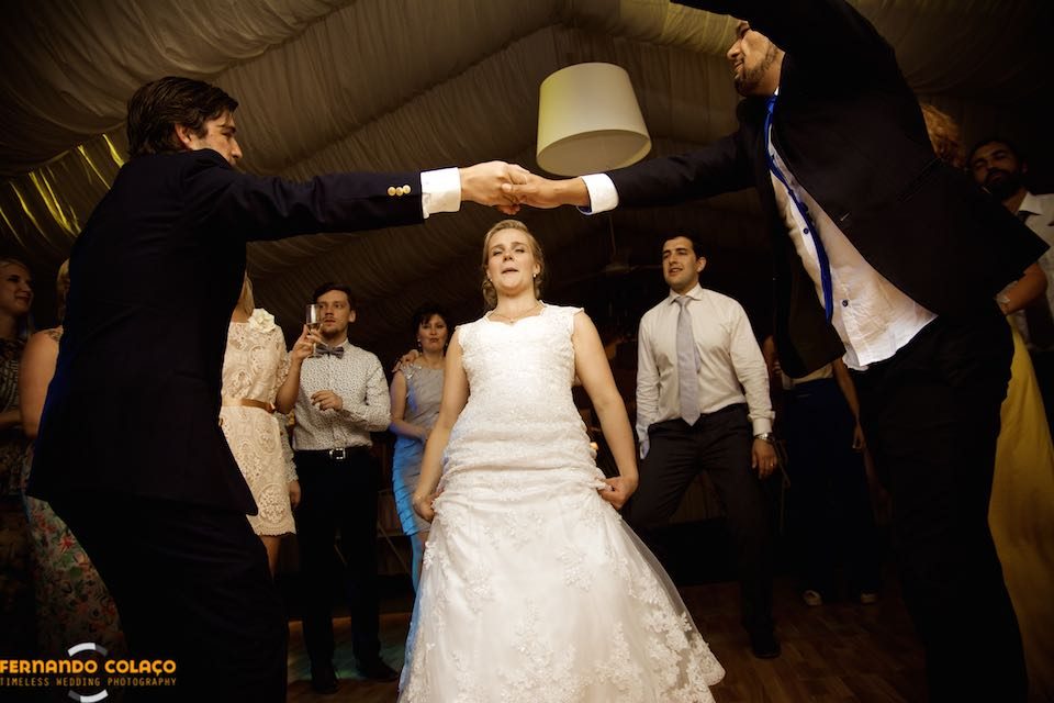 Two wedding guests make a bow with their arms for the bride to pass under at the wedding reception.