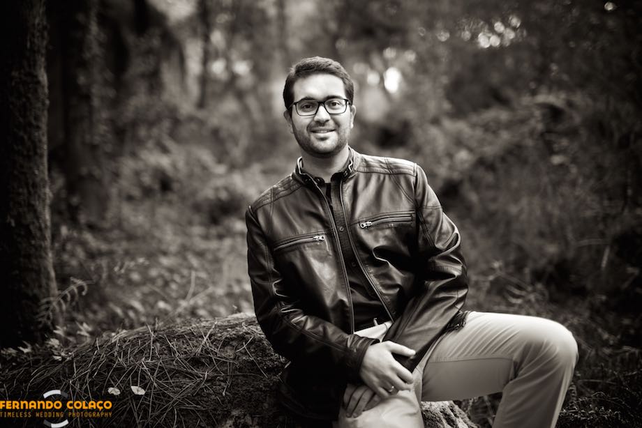 The groom, in the courtship session, sitting on a boulder of Peninha in Sintra, with the trees of the forest behind, looks towards the wedding photographer.
