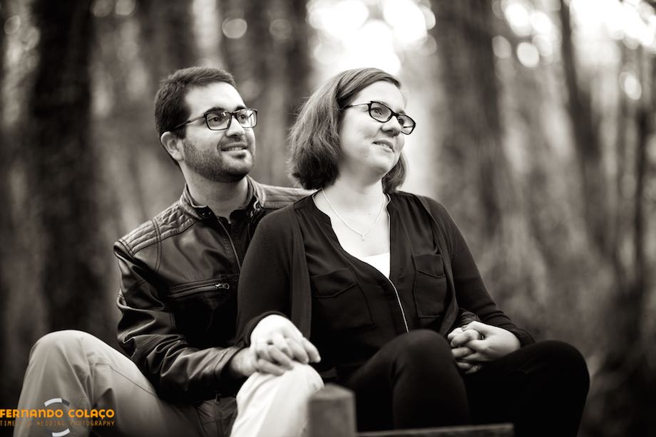 Sitting next to each other, the bride and groom look into the distance, with the trees of the forest, unfocused, in the background.