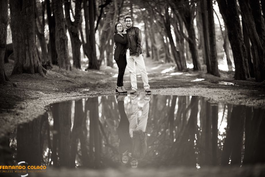 The couple in the pre-wedding session in front, and reflected, of a large puddle of water in the middle of the way in Peninha in Sintra.