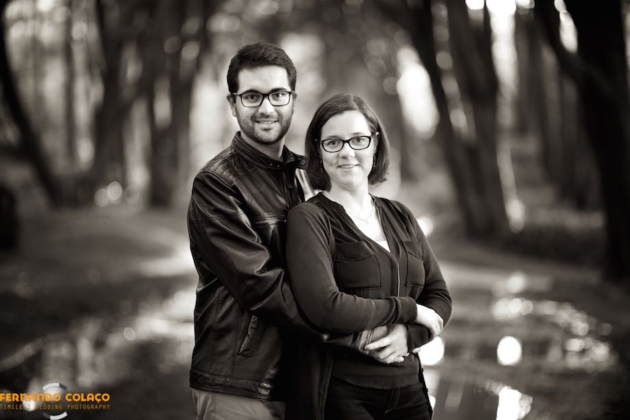 In the middle of the way and with the trees that flank it, out of focus, the bride and groom, hugging, look at the wedding photographer in the dating session.