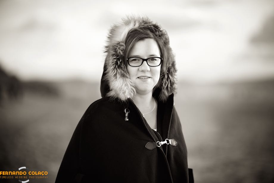 The bride, with a hood in her hair, with the sand of Guincho beach in Cascais, the sea and the sky in the background, blurred.