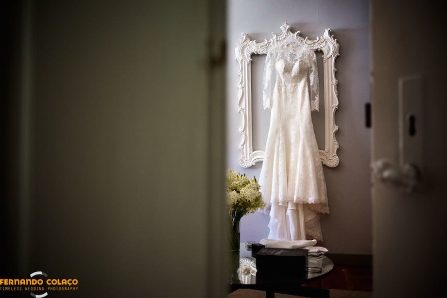 O vestido da noiva pendurado na parede sobre uma grande moldura vazia.