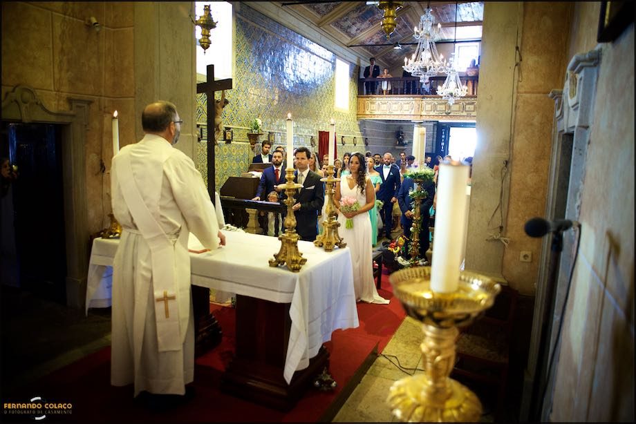 Os noivos no altar em frente ao padre com os convidados por detrás.