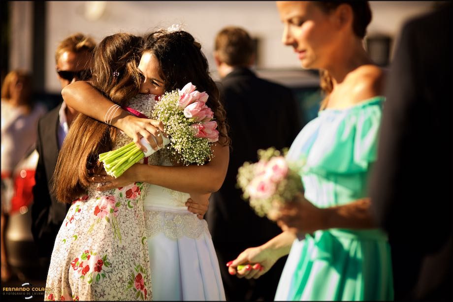 Noiva, com o ramo de flores na mão, abraça convidada à saída da igreja.