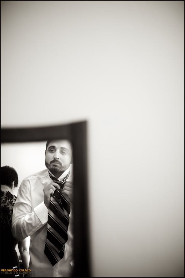 The groom tightens his tie in a mirror image.