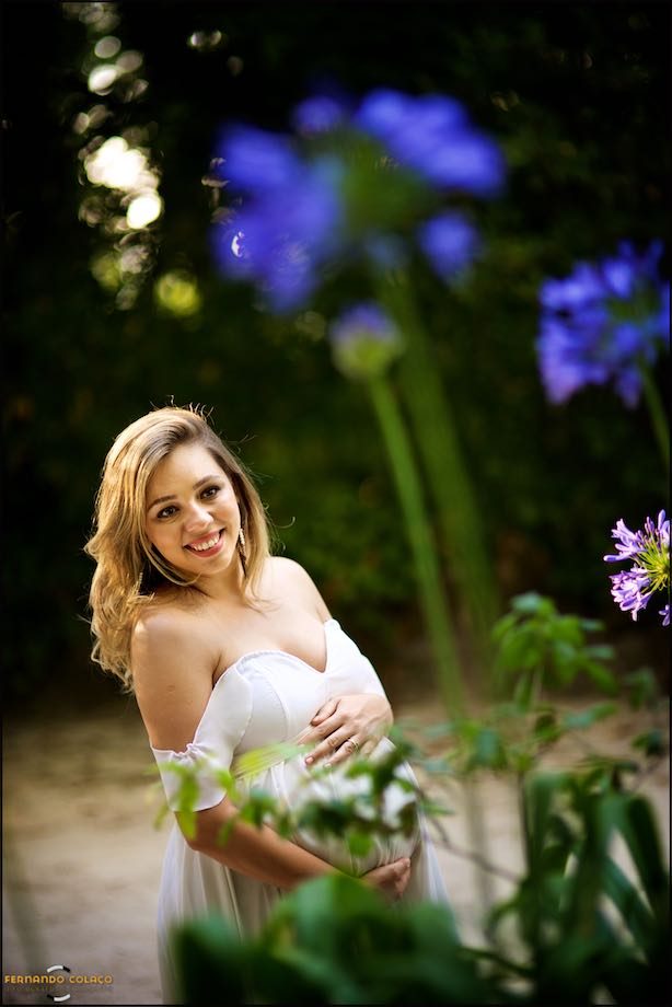 Grávida a sorrir perto de várias flores.