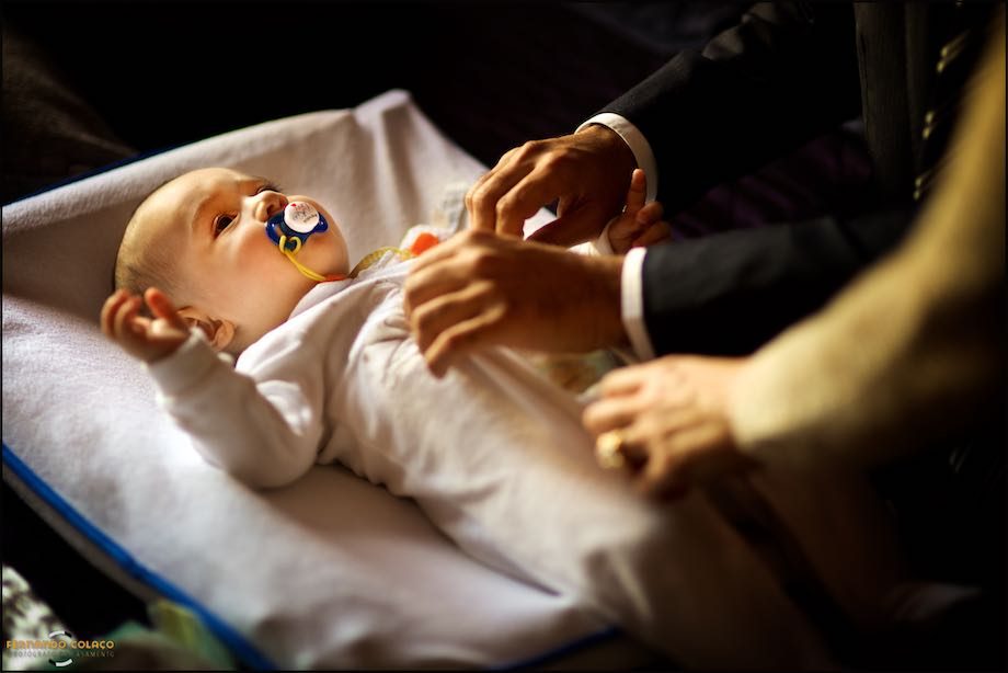 Menino, deitado, no começo do vestir do fato pra o batismo.