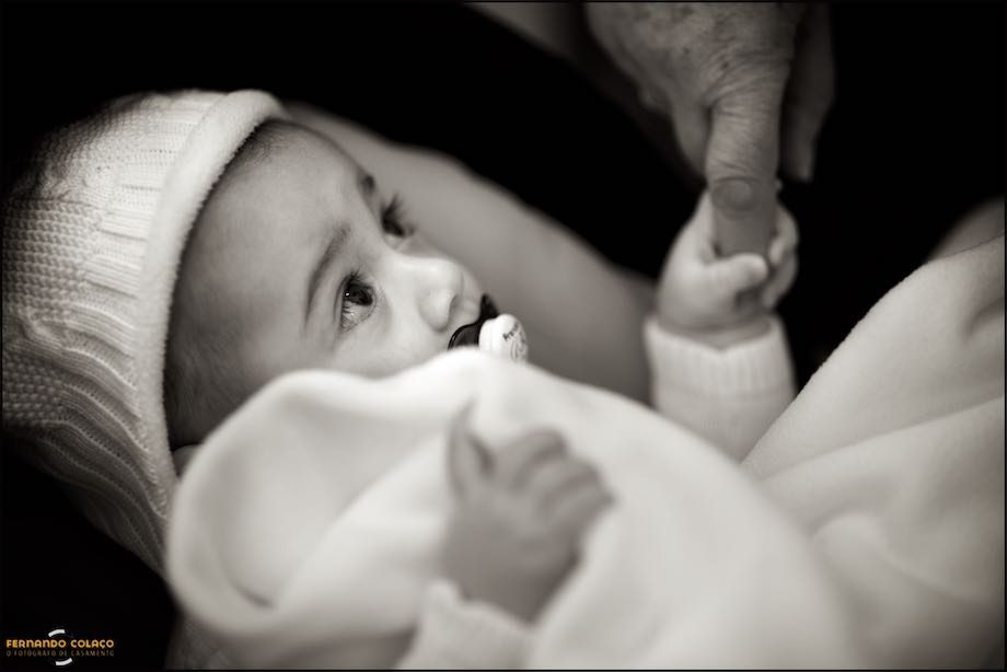 O bebé, envolto na sua mantinha já na igreja, aperta o dedo de uma senhora