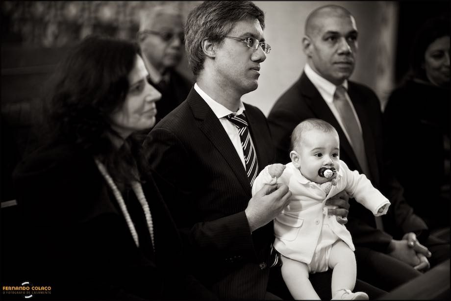 Já dentro da igreja para ser batizado, o bebé ao colo do pai, ao lado da mãe.