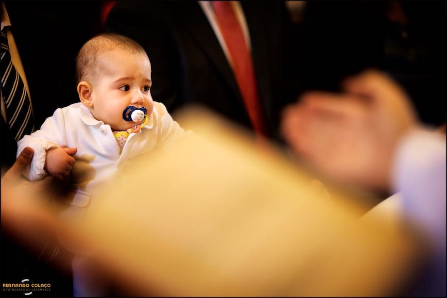 Mão do padre e livro litúrgico, desfocados em frente de menino no ritual do seu batismo.