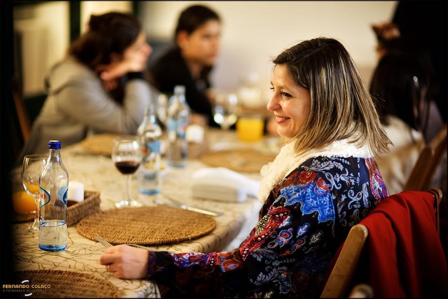 Uma convidada do batizado a sorrir, sentada à mesa.