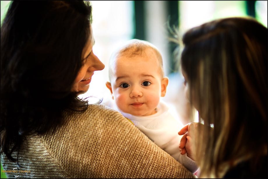 O bebé, já batizado, ao colo da mãe e alguém a falar com ele.