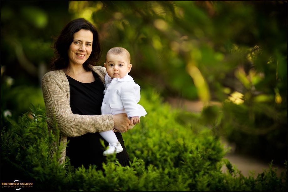 Mãe com o bebé sobre o verde das árvores do jardim.