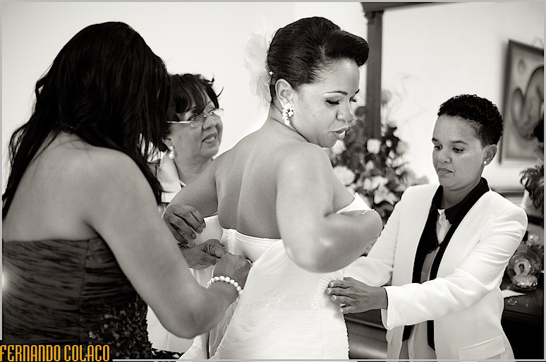 No meio de três mulheres, a noiva quando lhe apertam o fecho do vestido.