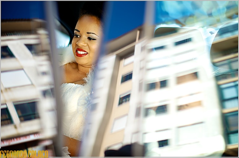 A noiva, vista por entre a porta do automóvel com os prédios de fronte reflectidos nos vidros das janelas, a partir para a cerimónia do casamento.