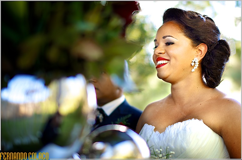 A noiva sorrindo junto de uma arranjo floral na mesa da cerimónia do casamento.