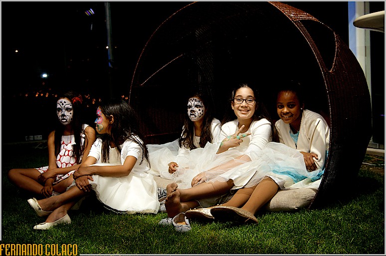 Um grupo de meninas, algumas de caras pintadas, sentadas debaixo de uma cabana no jardim da Quinta do Roseiral, durante a noite da festa do casamento Quinta do Roseiral.