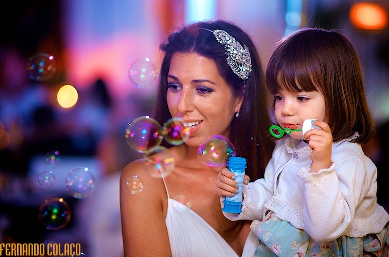 Menina, ao colo da noiva, faz bolas de sabão na festa do casamento no Wakiki na Praia da Sereia, pelo fotógrafo de casamento.