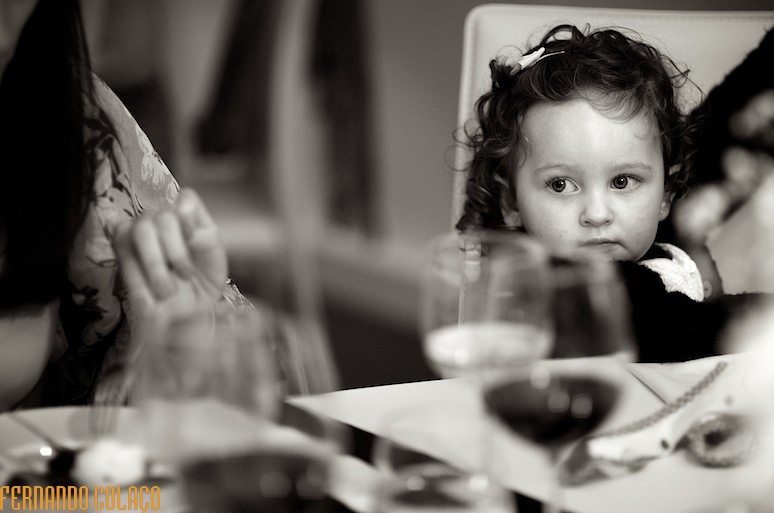 Menina pequenina sentada à mesa, num casamento.
