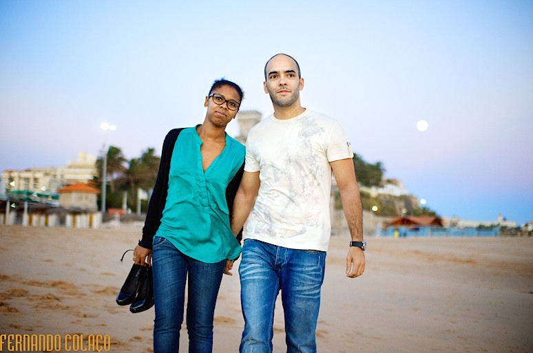 O noivo e a noiva em sessão de fotografias na Praia do Estoril, caminham no areal.