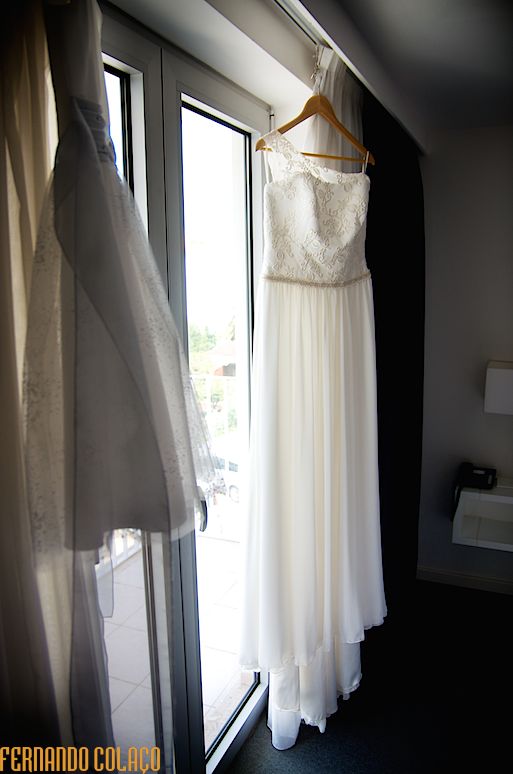 O vestido da noiva pendurado junto de uma janela.