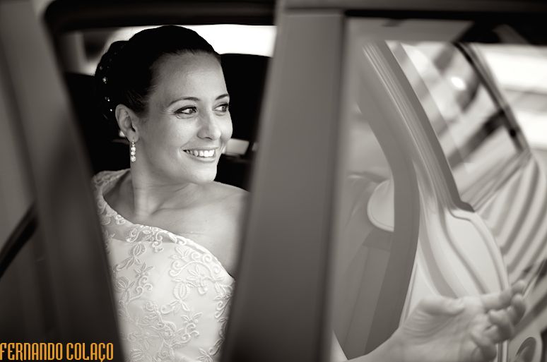 Dentro do automóvel a noiva olha para fora sorrindo.