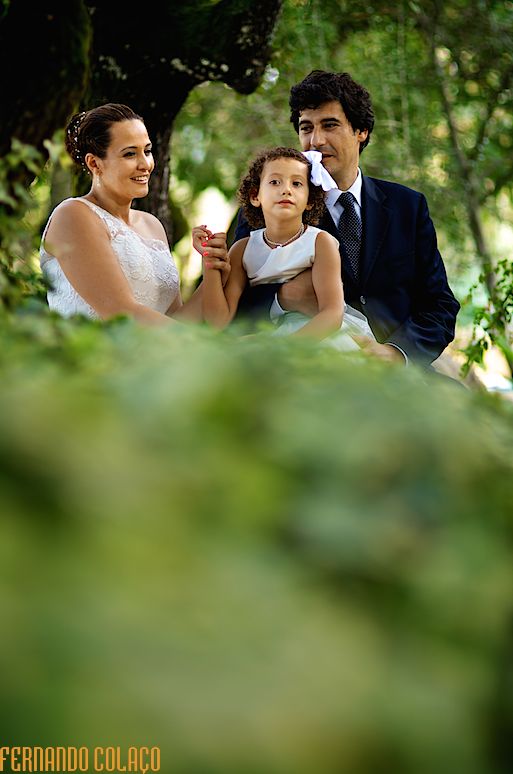 A família, pai, mãe e filha no meio das árvores do bosque, na sessão com o fotógrafo de casamento.