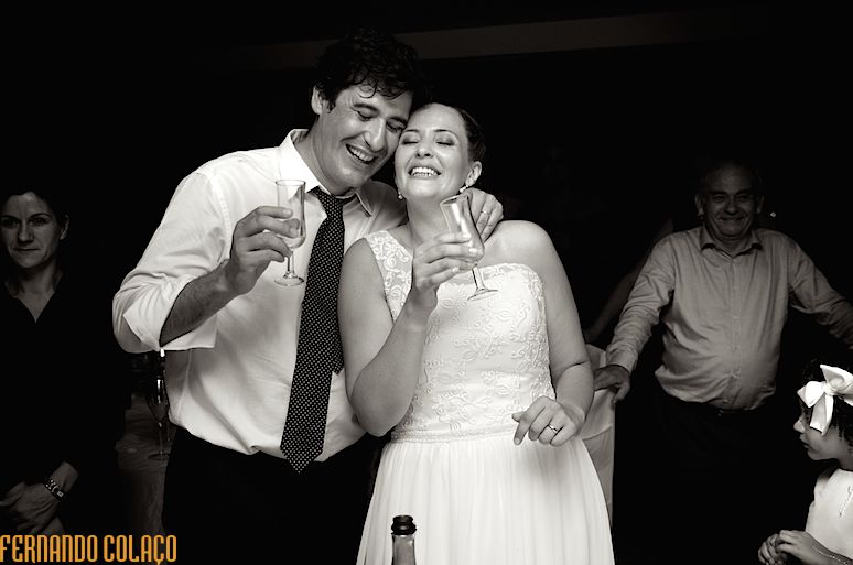 Depois do corte do bolo do casamento, os noivos, juntos, festejam com dois copos na mão.