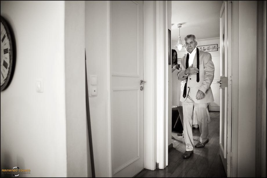 The bride's father, with his tie still unfastened, walking through a door of the house where he is preparing for his daughter's wedding.