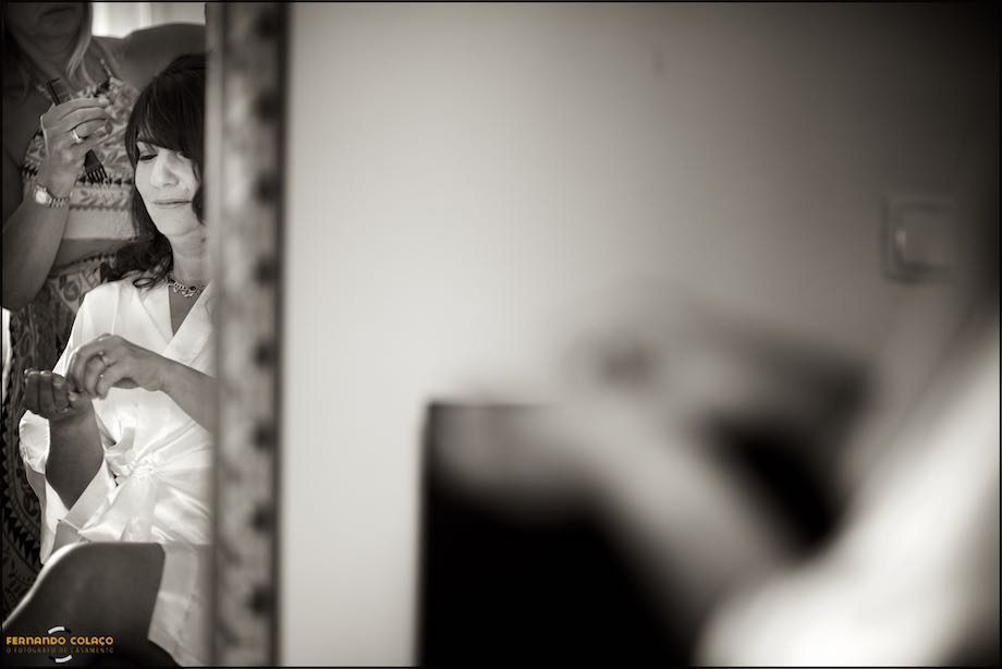In one part of the mirror, the bride has something in her hand while she is having her hair done.