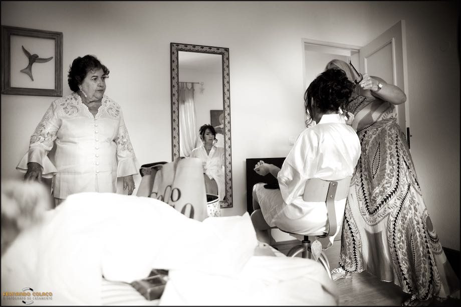 In the room where she is having her hair done, the bride, reflected in a mirror, with her mother and the hairdresser.