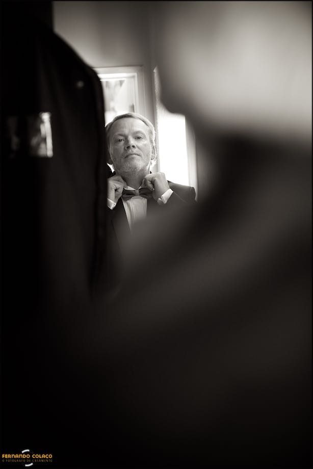 The groom, in the mirror, tightens the bow around his neck.