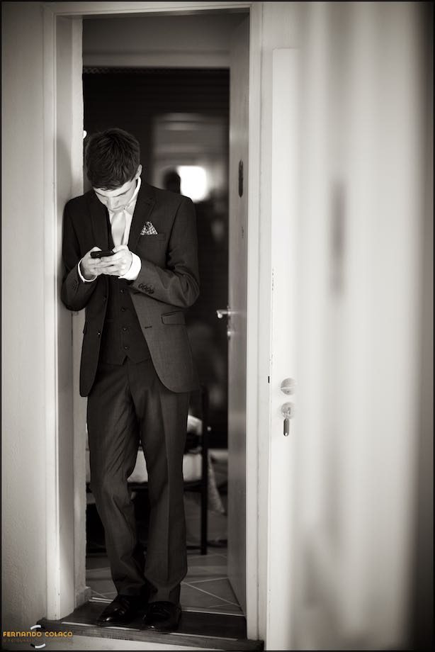 A young man, a wedding guest, standing by a door looking at his cell phone.